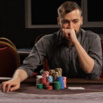 Handsome bearded man is playing poker sitting at the table in casino.