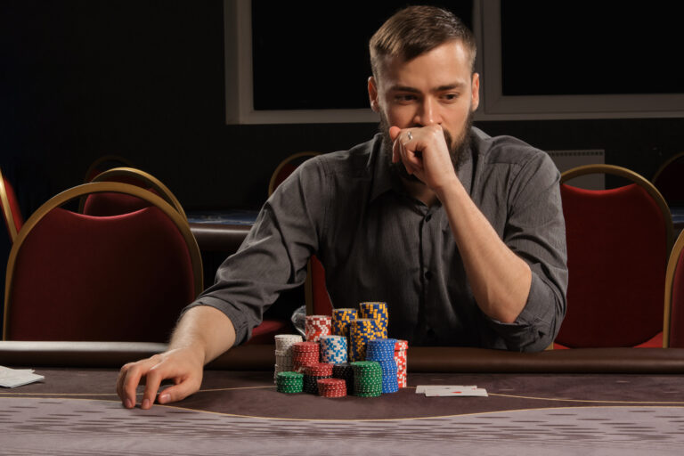 Handsome bearded man is playing poker sitting at the table in casino.
